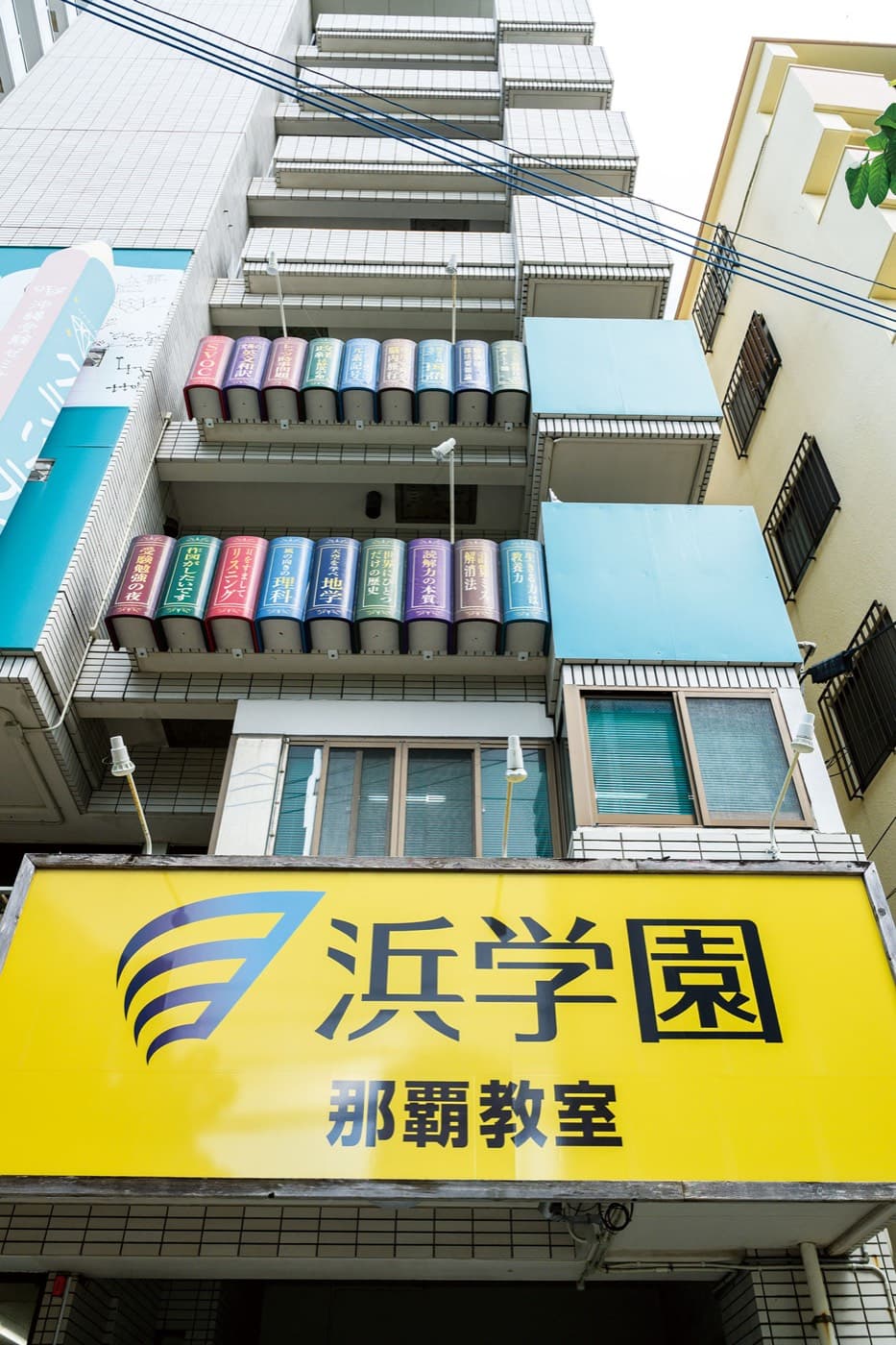 浜学園 那覇教室の外観。黄色い看板の上の外壁に、本の背表紙の形をした飾りが並ぶ