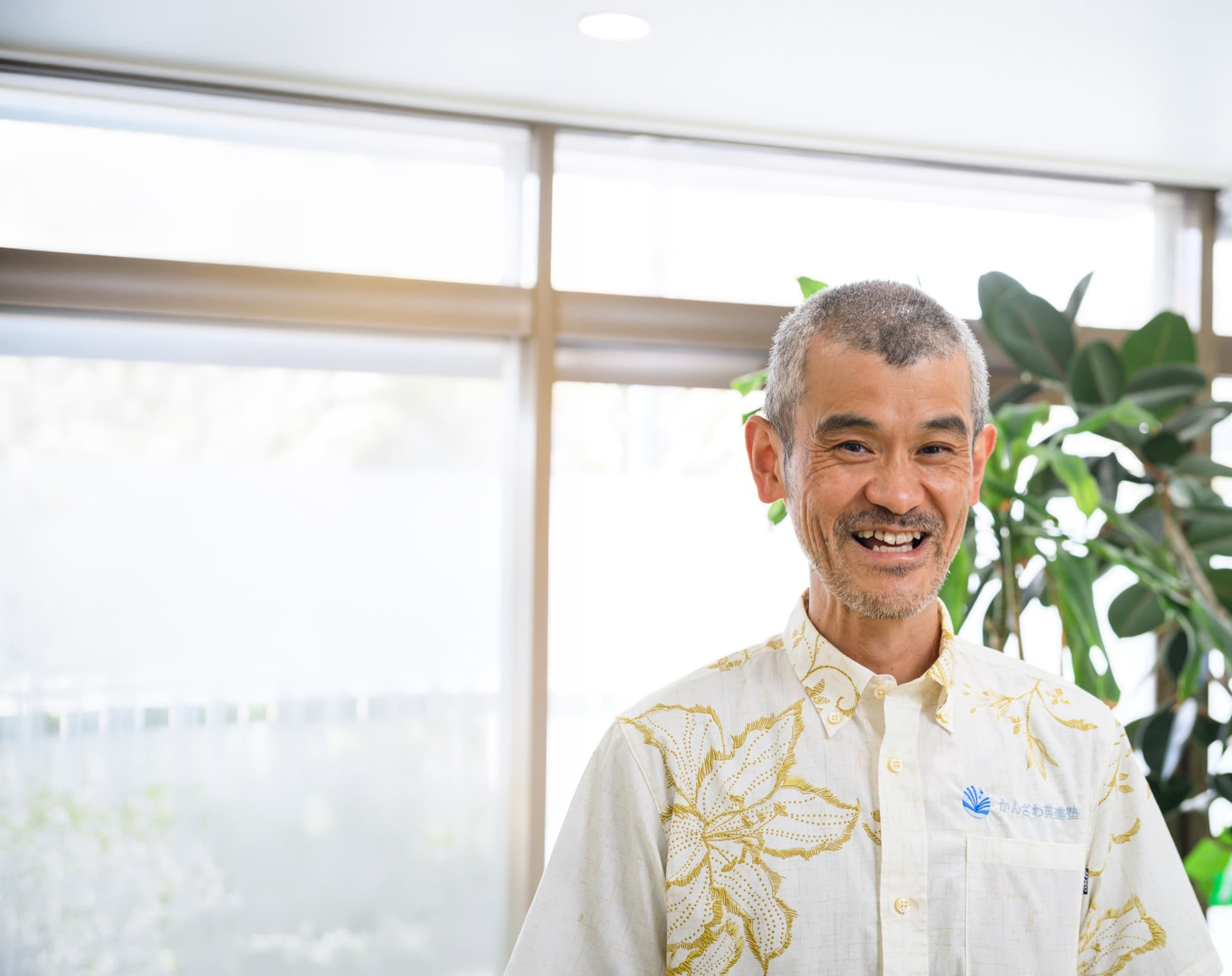 窓と観葉植物を背景に笑顔を見せる官澤治郎先生