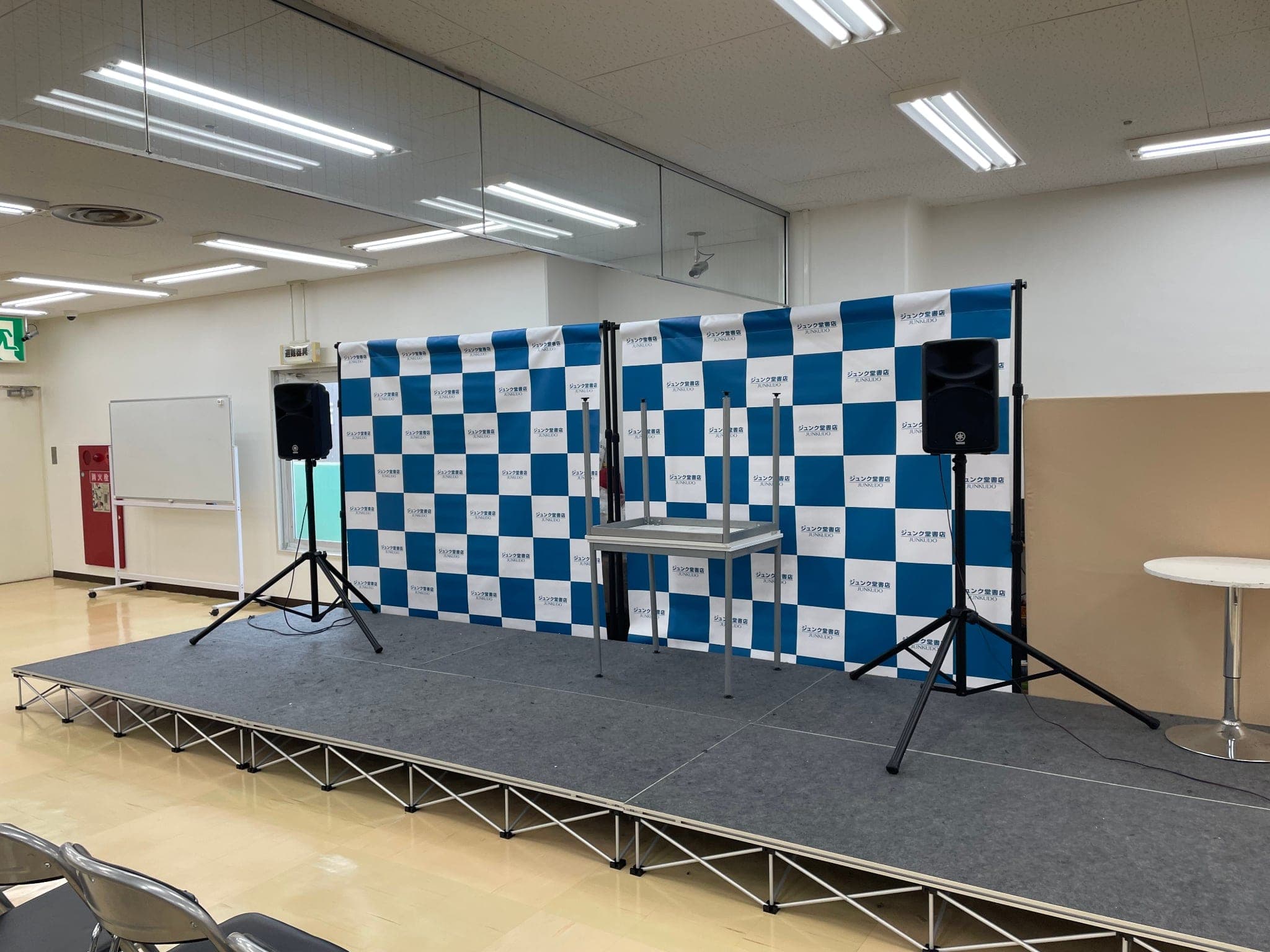 ジュンク堂書店のロゴが並ぶ背景パネルとスピーカーが置かれたイベントステージ