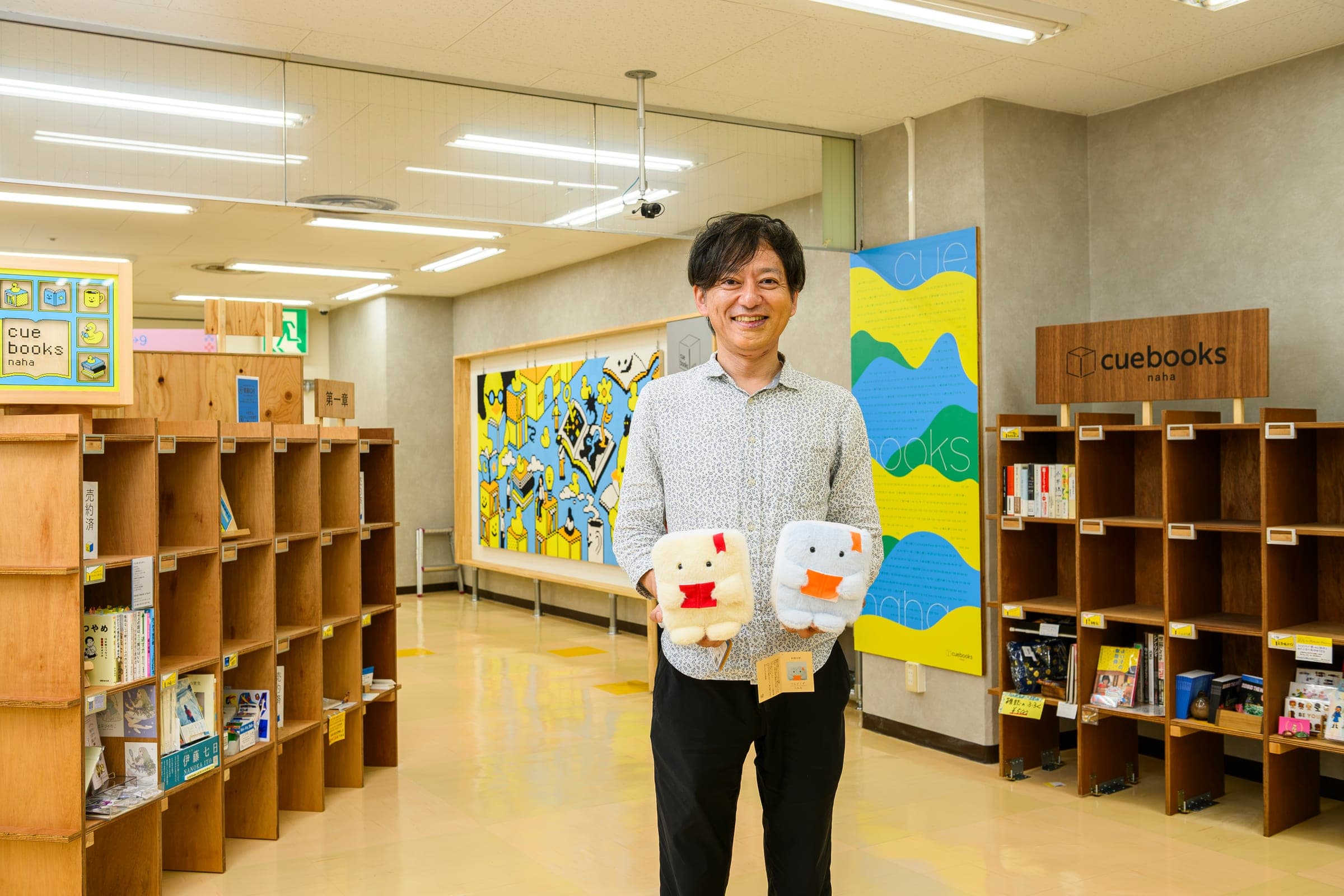 シェア本棚「cuebooks naha」の前で、オリジナルぬいぐるみ「つんどくず」を手にする森本浩平さん